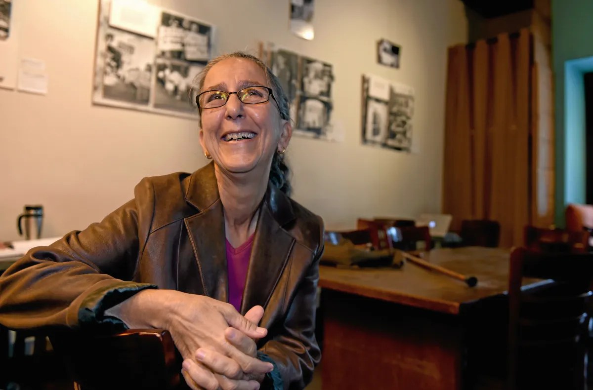 Lisa Hartouni smiling, seated in front of a wall of black-and-white archival community photographs.